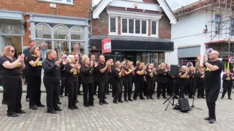 Thomas George / Rock Choir A group of people wearing black standing and clapping their hands while singing.