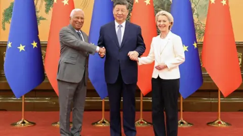 O presidente chinês da Reuters, Xi Jinping (Center), aperta as mãos do presidente do Conselho Europeu, Antonio Costa, e o presidente da Comissão Europeia, Ursula von der Leyen, no grande salão das pessoas em Pequim, em 24 de julho de 2025. Atrás deles há uma fileira de bandeiras da UE e da China.