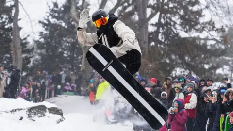 Shaun White does a snowboard flip in front of onlookers.