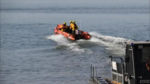 RNLI An orange lifeboat launches into the water.
