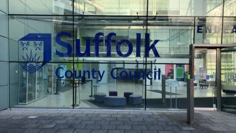 A glass fronted building which is the headquarters of Suffolk County Council. It reads Suffolk County Council in large blue writing 