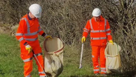 Guildford Borough Council Two people wearing hi-vis orange gear while litter picking.