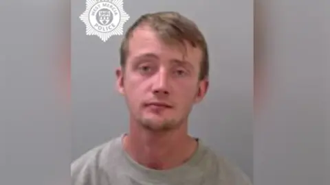 West Mercia Police A man with short brown hair swept to one side. He has short facial hair and is wearing a grey sweatshirt. 