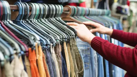 Getty A bargain-hunter wearing a red jumper looking through a tightly packed rail of trousers on hangars