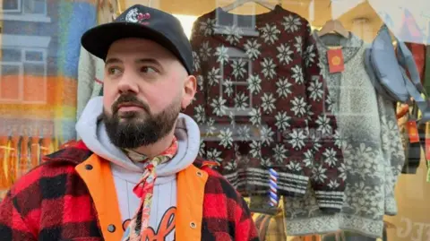 Alex Tribbensee Alex in front of his shop window containing retro items of clothing