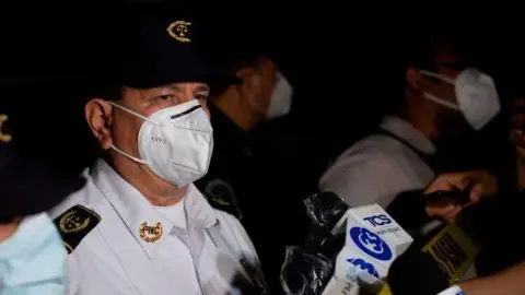 Getty Images National civil police director Mauricio Arriaza Chicas (C) speaks with the press at the crime scene where unknown men murdered six people inside a bar in La Isla neighborhood in San Salvador on 11 October 2020