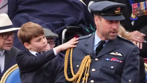 Prince Louis touches his dad William's shoulder as he wears military attire while sat next to him