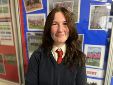 16-year-old Rebecca in a blue school jumper, white shirt and red tie