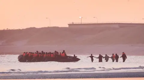 A group of people thought to be migrants wade into the water to board an approaching small boat in an attempt to reach the UK by crossing the English Channel.