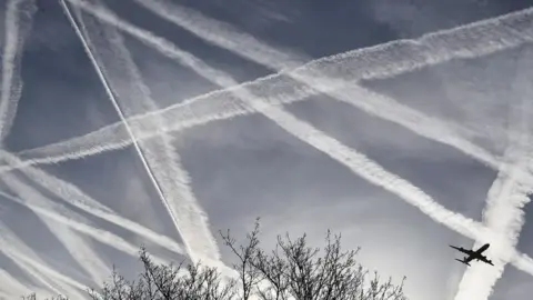 Reuters Aeroplane flies through a sky full of condensation trails