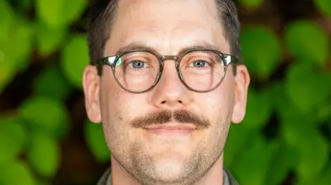A man with a moustache and glasses is smiling