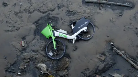 A Lime bike ar Blackwall Point, the Greenwich Peninsular foreshore of the Thames river at low-tide, on 18 February 2025