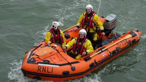 Richard Kirk Richard Kirk on board an RNLI lifeboat with two other crew members. The boat is sailing on the water. 