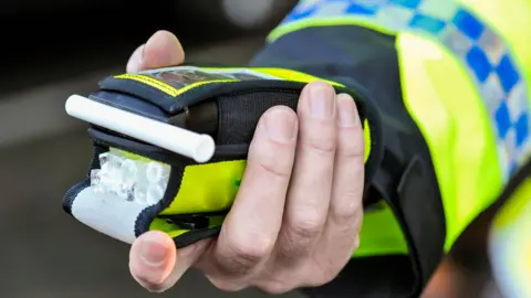 A police officer holds a roadside breathalyser alcohol breath test after taking a sample from a driver.