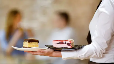 A stock image of a waitress holding two plates of cake. 