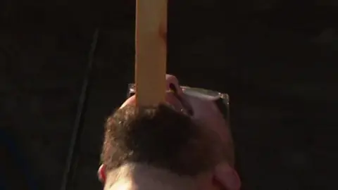 Man balancing plank of wood on his face