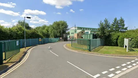 Google A road which enters into a gated site. Large buildings, which is used as the fire service's training centre, are in the distance.