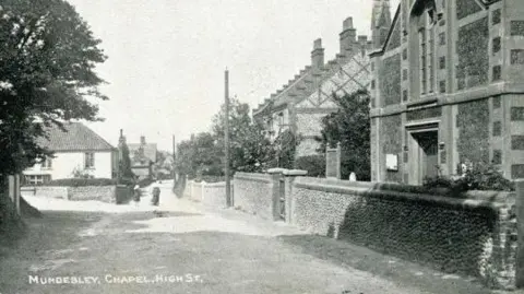 International Autograph Europe S.L The front of the postcard shows the chapel on the high street in Mundesley. It is a black and white photograph.