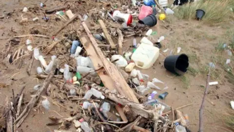 BEACH BUDDIES A sandy area is covered in litter. There are large plastic bottles, buckets and other containers.
