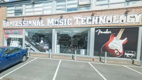 View of the PMT shop outside. There is a blue car in the car park.