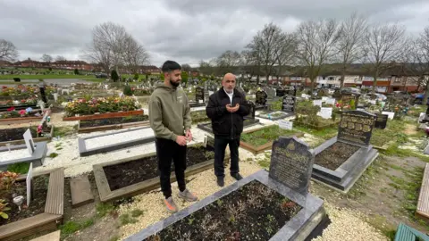 Mark Ansell/BBC Sahil Hussain and his uncle, Tariq Khan, saying prayers, also known as duas, at the graveside of one of their relatives at Dewsbury Cemetery