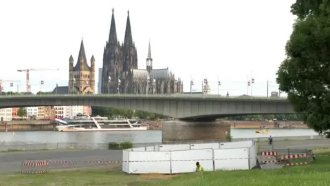 Reuters A person works by a cordoned off in a grassy area near a river, with Cologne Cathedral in the background