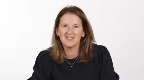Equity Release Council A middle aged woman with brown hair and brown eyes smiles at the camera, wearing a black blouse top and a silver necklace.
