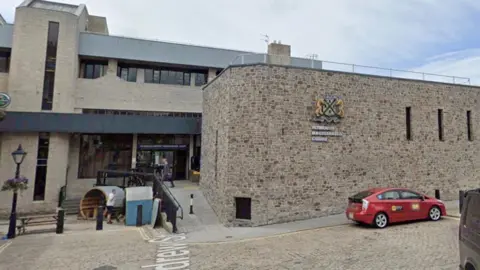 Google The front entrance to Plymouth Magistrates' Court. It is a stone building on a cobbled road, with a ramp built leading to the entrance. The logo can be seen on the front of the building.