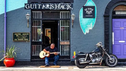 supplied A man sits on a sunny day playing  an acoustic guitar in the street