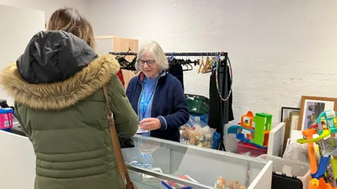 BBC A woman serving another woman at a charity shop