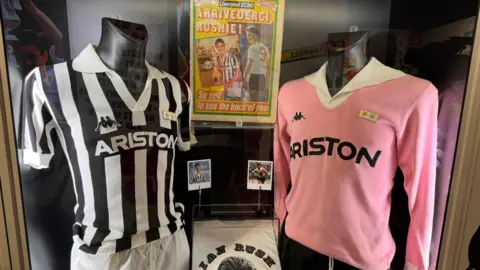 Black-and-white and pink Juventus kits displayed with Ian Rush photographs, souvenirs and newspaper memorabilia.