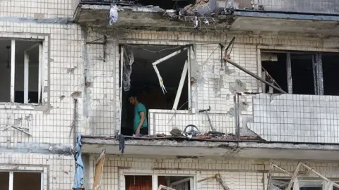 Residents clear debris at the site of a nine-storey residential building struck by a drone in Kyiv