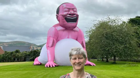 Frances King, standing in school field with giant inflatable man behind her