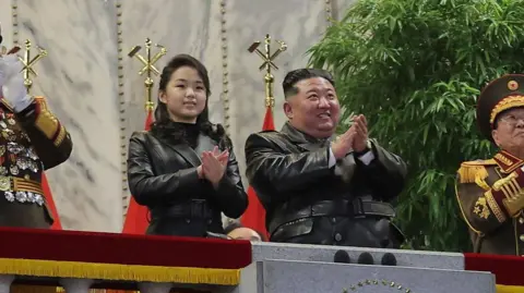 Reuters Kim Jong un standing next to his daughter, Ju Ae. They are wearing leather jackets and clapping, and flanked by officials in ceremonial uniforms