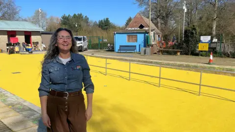 Councillor Marina Strinkovsky laughs in the sunshine in front of the newly-laid bright yellow surface.