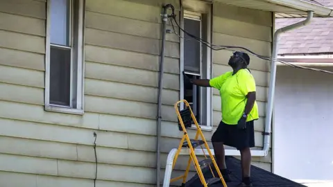 A person stands on a roof inspecting a power cable.