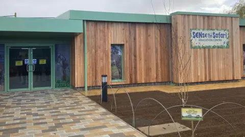 Nicola Haseler/BBC The outside of the new unit, which is single-storey and clad with wood panels and sage green edging. A sign says "SENse the Safari Education Centre".