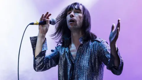 Getty Images Bobby Gillespie in 2013 wearing a silver shirt and singing on stage 