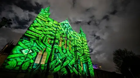 Salisbury Cathedral The facade of Salisbury Cathedral lit up for the Sarum Lights. Against a black and grey sky, a green maze pattern is projected onto the cathedral wall.