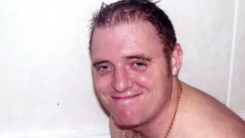 Supplied Ray McDonald sits against a white background. He appears to be either wet or is sweating and he is smiling at the camera. He is topless with a gold chain around his neck 