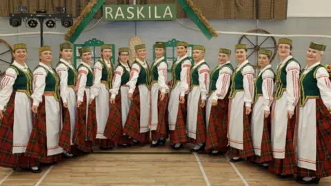 Jumped Up Theatre Dancers dressed in traditional Lithuanian attire - red checked skirts and white aprons with green vests and green headgear