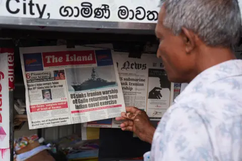 REUTERS A man checks the local newspaper, follwoing a submarine attack on the Iranian military ship, IRIS Dena, off the coast of Sri Lanka, in Galle, Sri Lanka, March 5, 2026. REUTERS/Thilina Kaluthotage