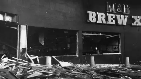 Getty Images A black and white photo of the aftermath of the explosion at one pub. Debris and glass can be seen on the floor with a sign of M&B Brew XI on the building
