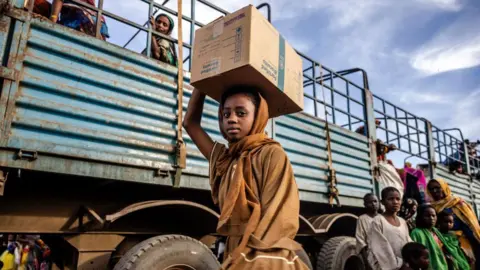 A Sudanese girl who have fled the war with her family carrying a box of belongings after arriving at a Transit Centre for refugees in Renk in South Sudan, in February 2024