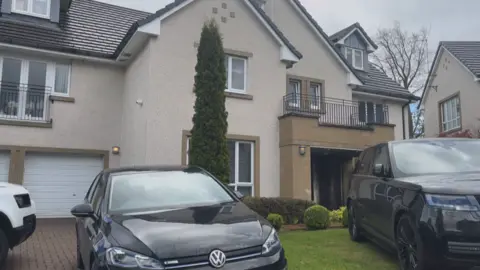 A general view of the house on Pitcairn Grove. Two cars are parked outside on the grass.