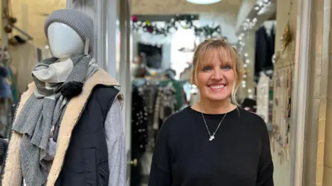 Gemma Dillon/BBC Deborah Bellamy owner of 'Hidden Wardrobe' in Corn Exchange in Leeds. She is standing in her shop front with clothes in the background. 