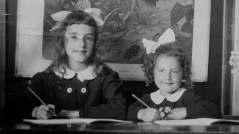 Two girls who were murdered in Auschwitz in 1943 sit together writing on exercise books in a black and white photo