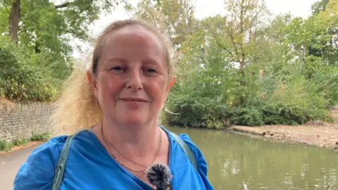 Ceri Dunning stands in front of the pond in St George park in Bristol, a small island is visible behind her