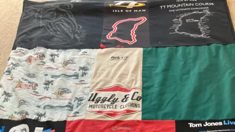 Clothing sewn together in squares to make a blanket. The words "Isle of Man TT", "motorcycle clothing" and "Tom Jones Live" can be seen.
