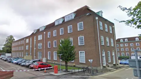 A Google Street image of West Sussex County Council's County Hall in Chichester. It is a four-storey red-bricked building with several white-framed windows.